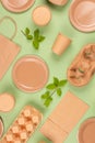 Flat lay composition with eco-friendly tableware and kraft paper food packaging on green background. Sustainable