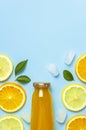 Flat lay composition with glass bottles of juice or fresh, slices of fresh lemon and orange, green leaves, ice cubes on blue Royalty Free Stock Photo