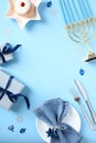 Flat lay composition with Hanukkah symbols, menorah, plate with napkin and cutlery on pastel blue table. Hanukkah food concept