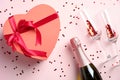 Flat lay composition with a heart-shaped box decorated with red ribbon, champagne bottle, glasses with confetti on pink background Royalty Free Stock Photo