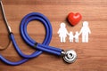 Flat lay composition with heart, stethoscope and paper silhouette of family on wooden background. Royalty Free Stock Photo