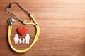 Flat lay composition with heart, stethoscope and paper silhouette of family on wooden background, space for text. Royalty Free Stock Photo