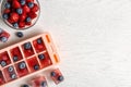 Flat lay composition with ice cube tray and berries on wooden background.