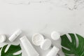 Flat lay composition made of cosmetic bottles, cream jars, green tropical leaves on marble background