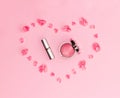 Flat lay composition with makeup products and pink flowers in a shape of heart on pink background. Royalty Free Stock Photo