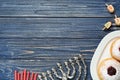 Flat lay composition of menorah, red candles, dreidels with He, Pe, Nun, Gimel letters and sufganiyot on blue wooden table, space Royalty Free Stock Photo