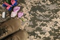 Flat lay composition with boots and flowers on camouflage background, space for text. Armed Forces Day