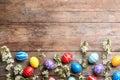 Flat lay composition with painted Easter eggs and blossoming branches on wooden background.