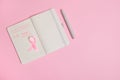 Flat lay composition of a pink ribbon, on opened notepad with inscriptions reminding of a medical check-up. October 1st, World