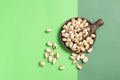 Flat lay composition of pistachios on wooden spoon and dish on green background with copy space