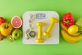 Flat lay composition of scales, dumbbells and tape measure, plate with fruits and vegetables on green background Royalty Free Stock Photo