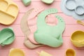 Flat lay composition with silicone baby bibs and plastic dishware on pink wooden background