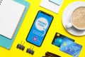 Flat lay composition of smartphone with activated promo code, credit cards and stationery on yellow table