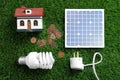 Composition with solar panel, house model, light bulb and coins on green grass Royalty Free Stock Photo