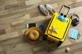 Flat lay composition with suitcase, protective masks, antiseptic spray and personal items on wooden floor. Travelling during