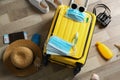 Flat lay composition with suitcase, protective masks, antiseptic spray and personal items on wooden floor. Travelling during