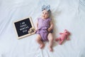 Flat lay composition of three months old baby girl laying down on white background with letter board and teddy bear. Royalty Free Stock Photo