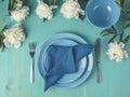 Flat lay composition with white peony flowers, empty plate with napkin and cutlery on wooden turquoise table surface, festive flat Royalty Free Stock Photo