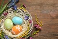 Flat lay composition of wicker nest with painted Easter eggs and flowers on wooden table Royalty Free Stock Photo