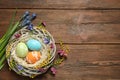 Flat lay composition of wicker nest with painted Easter eggs and flowers on wooden table Royalty Free Stock Photo