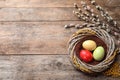 Flat lay composition of wicker nest with painted Easter eggs and willow on wooden table