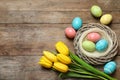 Flat lay composition of wicker nest with painted Easter eggs and tulips on wooden table Royalty Free Stock Photo