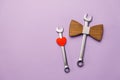 Flat lay composition with wooden bow tie, little red heart, two combination wrenches on pastel violet background with copy space.