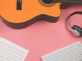 Flat lay of computer keyboard, headphones, blank music sheet and acoustic guitar on pink background. Music online learning and