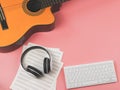 Flat lay of computer keyboard, headphones, blank music sheet and acoustic guitar on pink background. Music online learning and