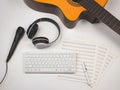 Flat lay of computer keyboard, headphones, microphone, blank music sheets and acoustic guitar on white background. Online music Royalty Free Stock Photo