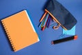 Flat lay with a copybook, organizer, colorful pencils and pencil case with falling out school supplies , in blue and orange Royalty Free Stock Photo