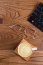 Flat lay cup of cappuccino with glasses and keyboard.