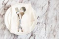 Flat lay is cutlery, fork and knife on a napkin on an empty white plate on a marble table Royalty Free Stock Photo