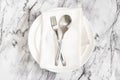 Flat lay is cutlery, fork and knife on a rustic napkin on an empty white plate on a marble table Royalty Free Stock Photo