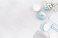 Flat lay of different cosmetics products and accessories of silver, pastel blue and white color with small flowers on white wooden