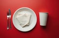 Flat lay of disposable tableware on red surface. Paper plate with napkin and cup. Fork and knife. Concept of eco friendly Royalty Free Stock Photo
