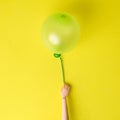 Flat lay of doll hand holding balloon with string abstract on yellow