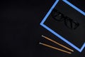 Flat lay of eyeglasses on an empty blank chalkboard and two wooden pencils on black background with coy space