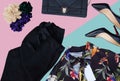 flat lay fashion set of black trausers, floreal shirt, black leather clutch bag, black hills and flower pins over pink and