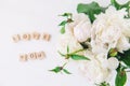 Flat lay focus on fresh bouquet of white peonies and blurred Love you lettering spelled in wooden blocks on light background. Love