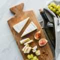 flat lay with food composition of camembert cheese on cutting board and wine on white