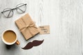 Flat lay gift box with label Happy Fathers Day, mustache, glasses, cup of coffee on wooden table. Top view Father`s day