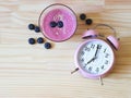 Flat lay of a glass blueberry smoothie and pink vintage alarm clock 7 o`clock on wooden table background Royalty Free Stock Photo