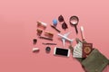 Flat lay of green leather woman shoulder bag open out with cosmetics, accessories , smartphone , money and passport on pink