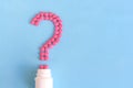 Question mark from pink pills next to white bottle on blue background Royalty Free Stock Photo