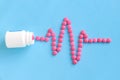 Heart rhythms from pink pills next to white bottle on blue background Royalty Free Stock Photo