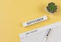 Flat lay of habit tracker book with pen, succulent plant pot and wooden calendar september on yellow background