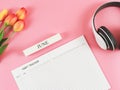 flat lay of habit tracker book with wooden calendar June, headphones and tulips on pink background