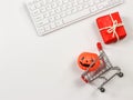 Flat lay of  Halloween pumpkin on shopping cart, red gift box and computer keyboard  on white background with copy space. Royalty Free Stock Photo