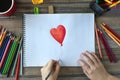 Flat lay of hands drawing a heart with colored pencils on white paper. Art studio workplace concept